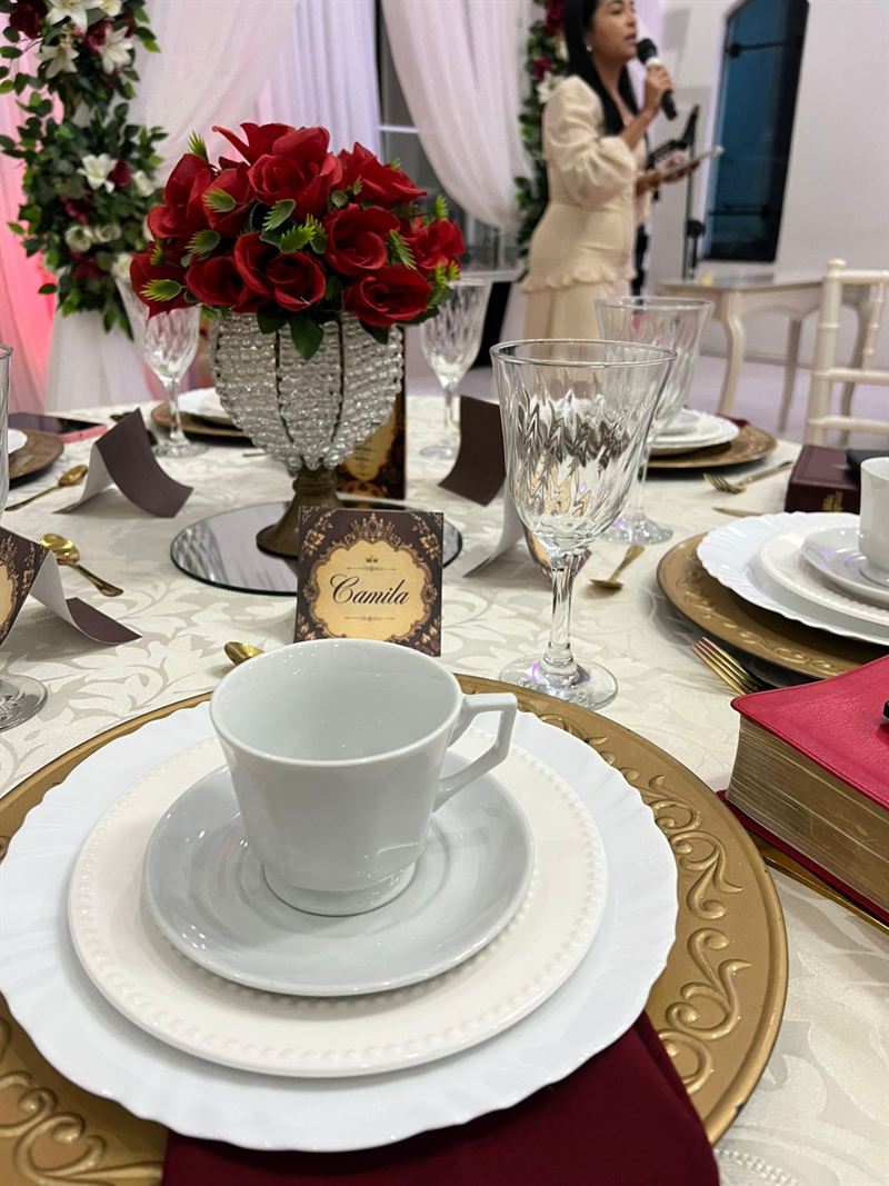 Lugar posto na mesa com xícara, taça, flores e o cartão com o nome da convidada
